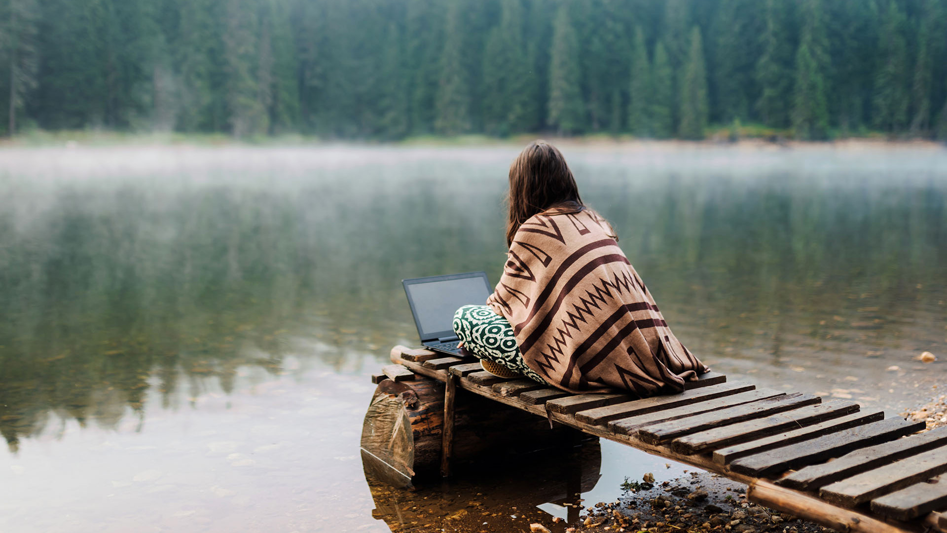woman sitting by the water using a laptop
